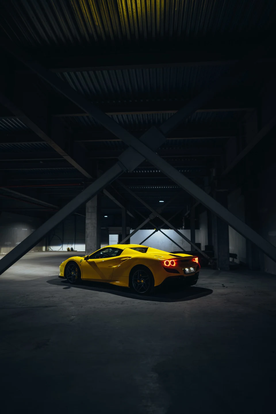 A yellow Ferrari beneath the steel structure of a dark industrial building
